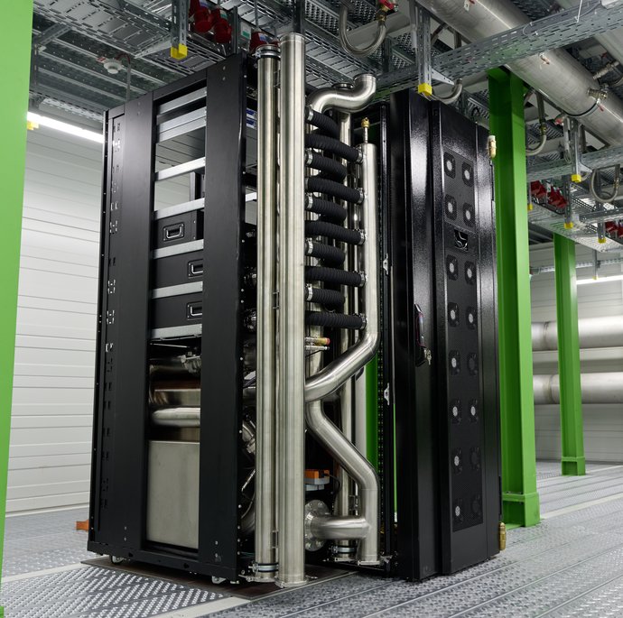 In einem industriellen Raum mit grünen Metallsäulen steht ein schwarzer Server mit silbernen Verrohrungen.