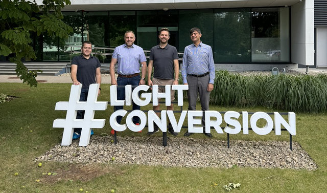 Four man stand on a green meadow in front of a building, behind the writing "Light Conversion".