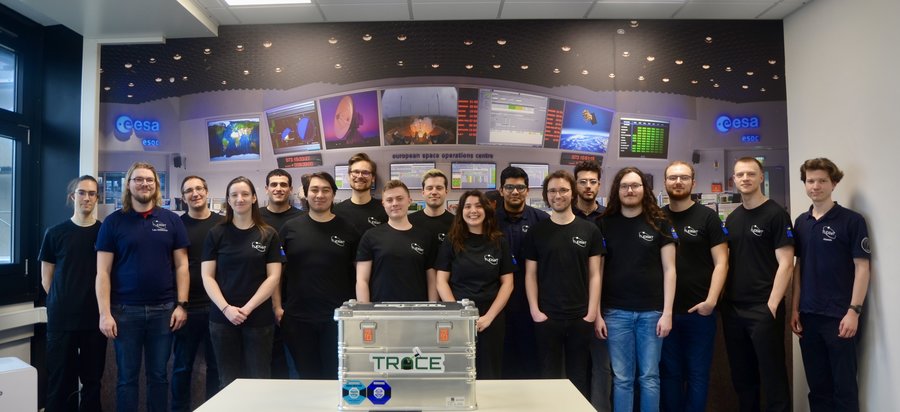 Eine Gruppe Personen steht hinter einer silbernen Transportbox.